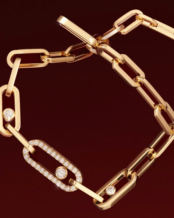 Close-up of a gold link chain bracelet with diamond-set links against a dark burgundy background.