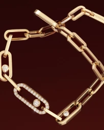 Close-up of a gold link chain bracelet with diamond-set links against a dark burgundy background.