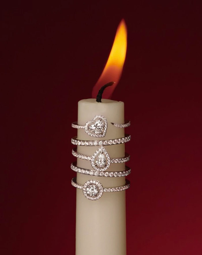 Close-up of a white candle stacked with diamond rings against a deep red background