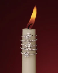 Close-up of a white candle stacked with diamond rings against a deep red background