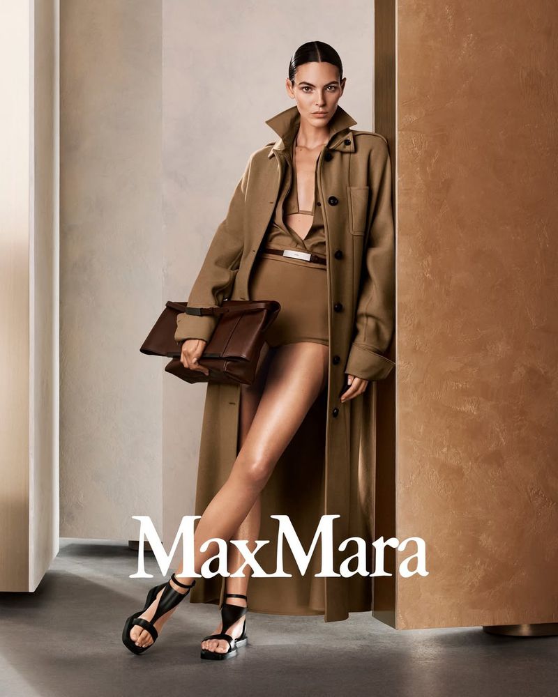 Fashion shot of a woman in tan outfit and coat holding a purse, posed against a neutral wall. Max Mara logo is visible.