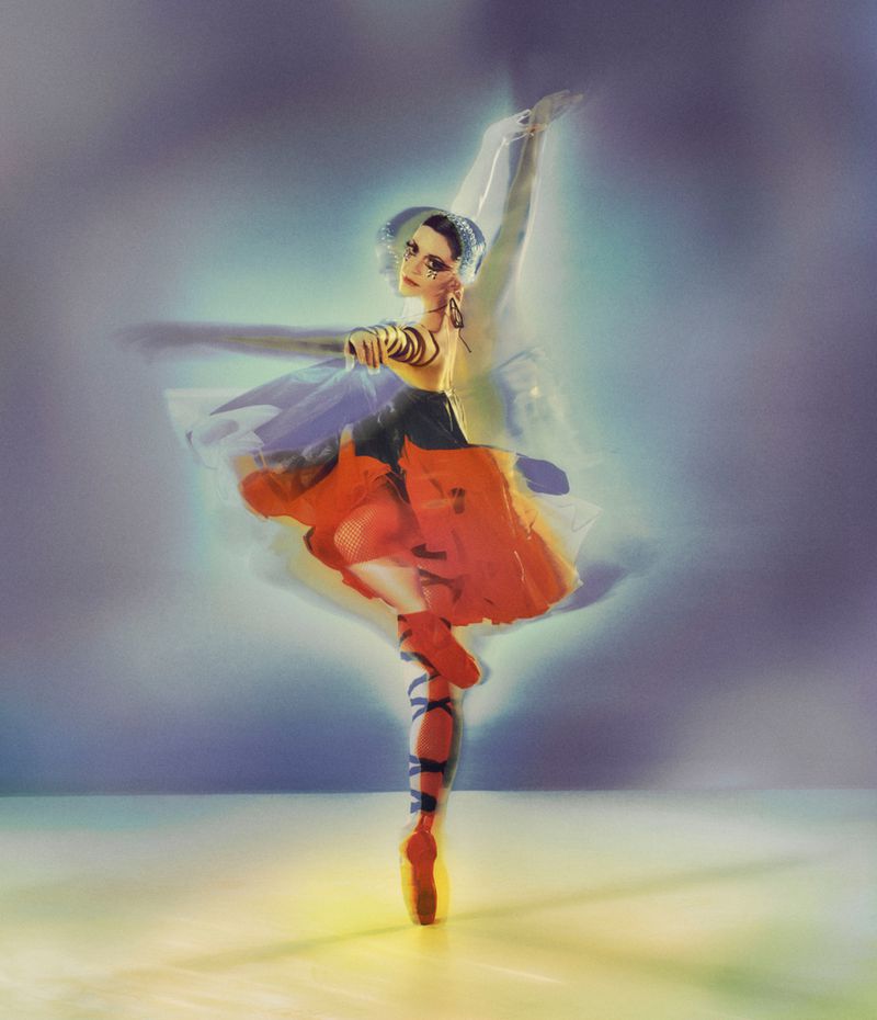 Ballet dancer en pointe in motion, wearing orange tutu and pointe shoes, with flowing fabric and a light, artistic background.