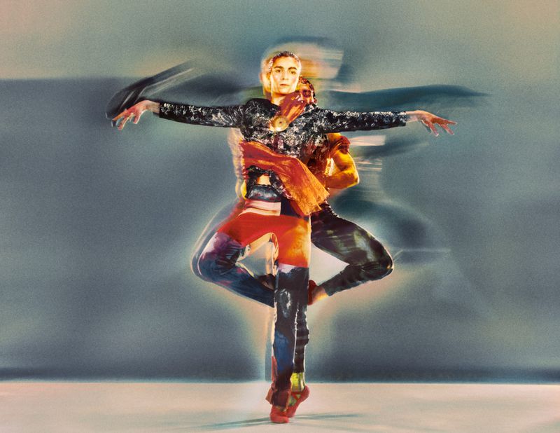 Dance performance art featuring an adult female in motion, wearing a patterned top, jeans, and shoes, against a blurred background.