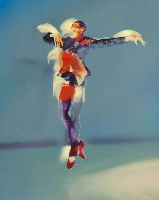 Motion blur dance photography: Ballet dancer in pointe shoes and dark suit, leaping mid-air against soft blue studio background.