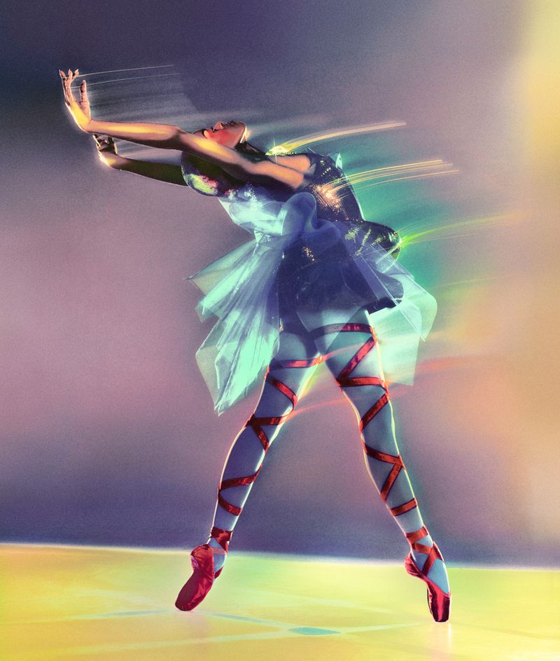 A ballet dancer in a blue tutu and red pointe shoes performs a ballet move in a brightly lit studio with a motion blur effect.