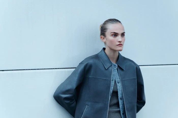 Model wearing a dark leather jacket over a textured sweater leaning against a pale wall for Samsoe Samsoe