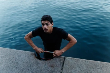 Young man in dark t-shirt holding a metal ring by the water edge for Samsoe Samsoe