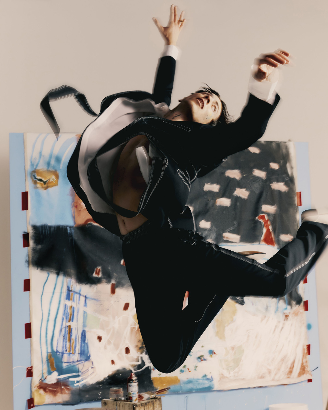 Man in a black suit mid-air leaping in front of an abstract painted canvas backdrop for T Magazine