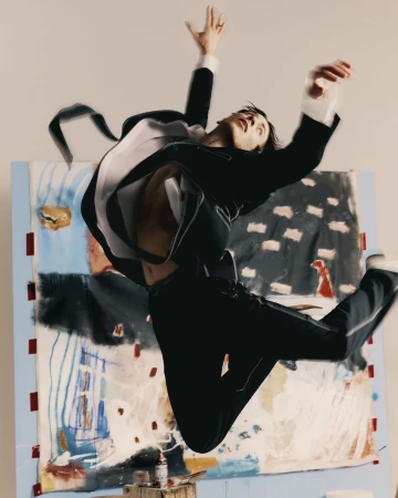 Man in a black suit mid-air leaping in front of an abstract painted canvas backdrop for T Magazine