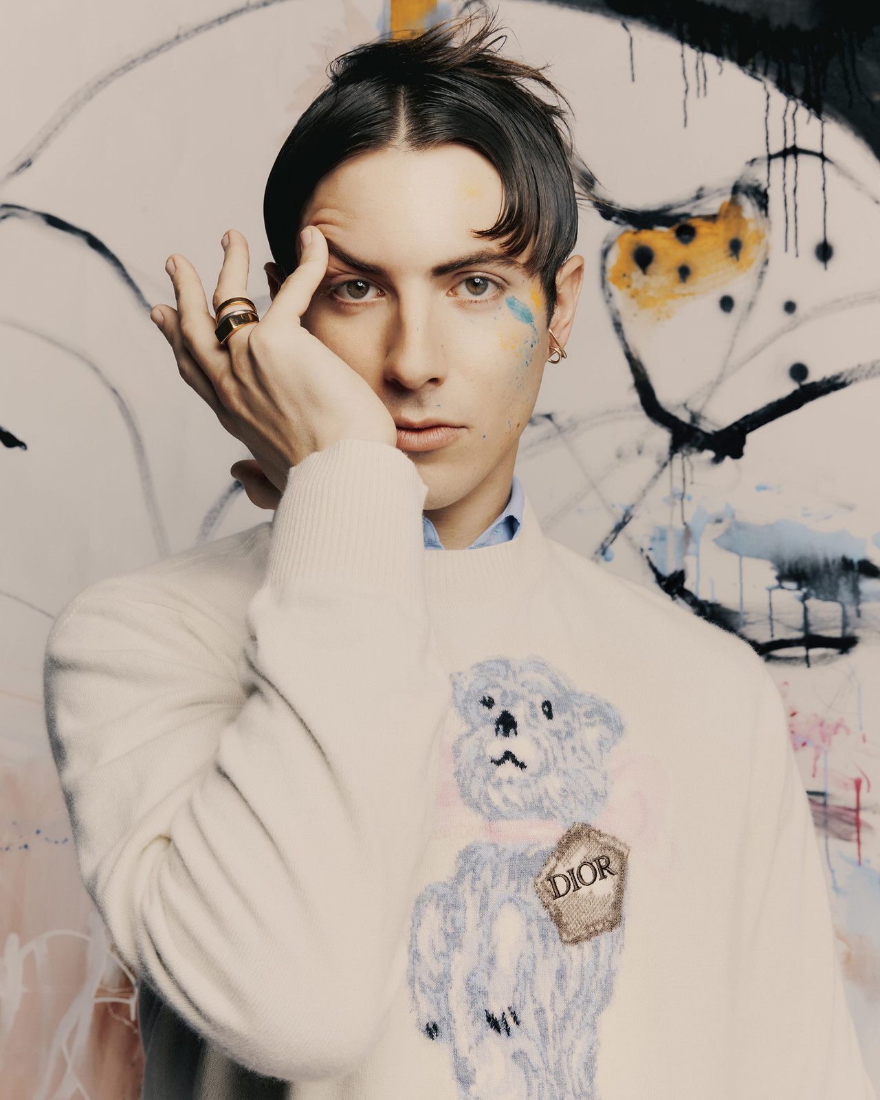 Portrait of a young adult male with dark hair, wearing a sweater with a bear design, posing against a painted background in a photo studio.