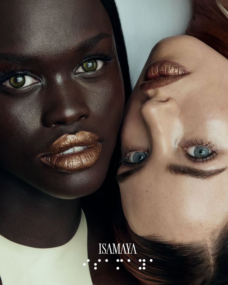 Close-up beauty shot of two fashion models, one Black woman and one Caucasian woman, both wearing shimmering bronze lip makeup.