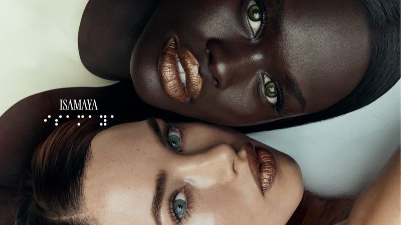 Close-up beauty shot showcasing two women with contrasting skin tones and glossy bronze lipstick against a light gradient backdrop.