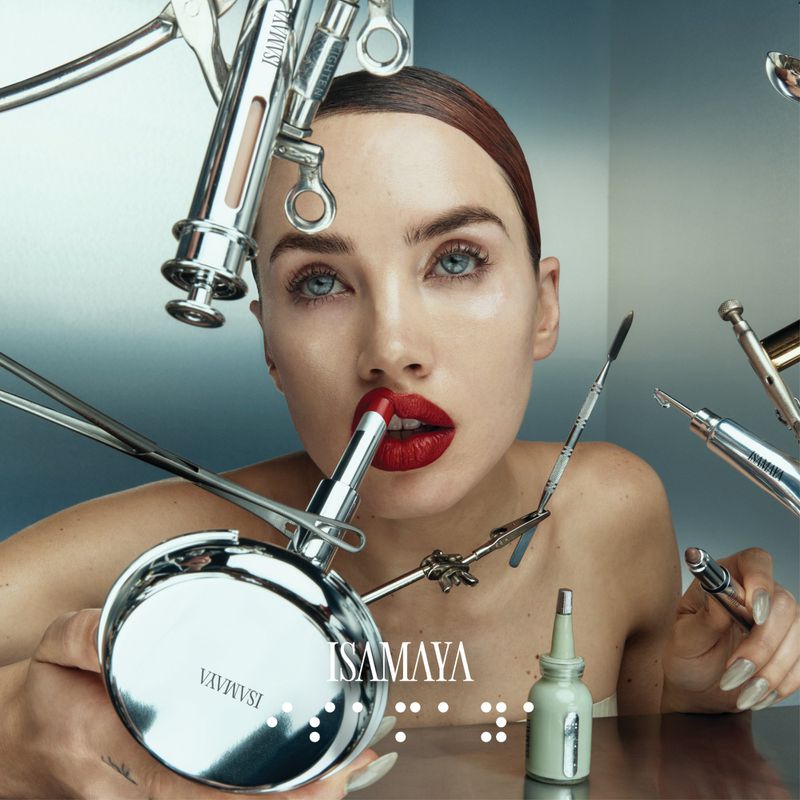 Beauty shot of a young woman with red lipstick. She is surrounded by vintage-style cosmetic tools and holding a makeup compact.