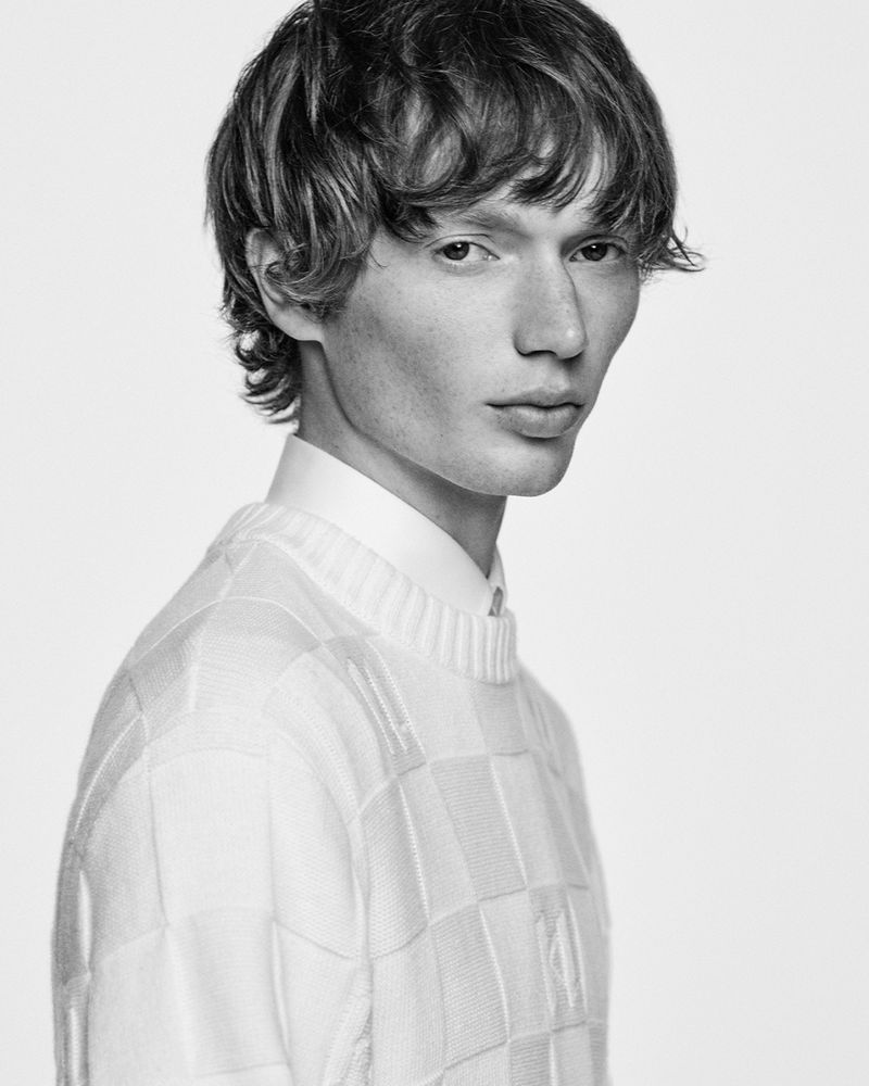 Monochrome portrait of a young male model wearing a textured white crewneck sweater against a seamless light background.