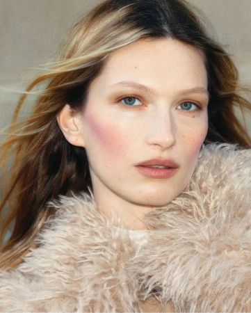 Close-up portrait of model Liz Kennedy wearing a textured faux-fur coat with wind-blown blonde hair.