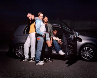 Four diverse models posing outdoors at night beside a parked grey hatchback car for Puma King project photographed by Ewen Spencer.