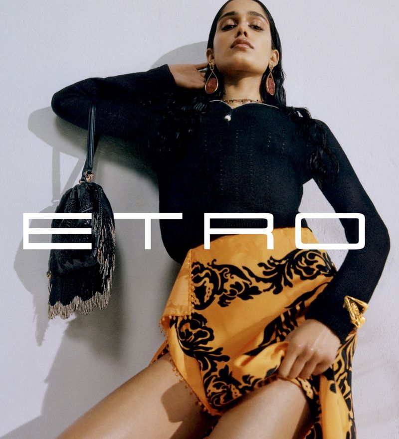 Woman poses with patterned skirt and black top, accessorized with earrings and a small bag, in a studio setting with the ETRO logo.