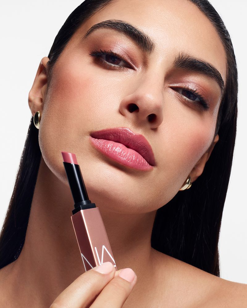 Close-up of woman with lipstick, showcasing NARS makeup. Model poses in bright lighting, emphasizing the product's color and texture.