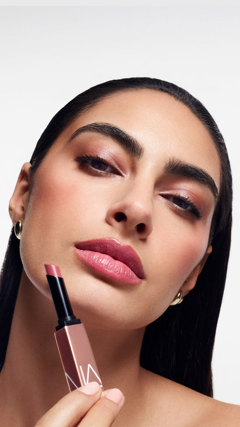 Close-up shot of a woman with makeup holding a lipstick in front of a white background, showcasing beauty and cosmetics.