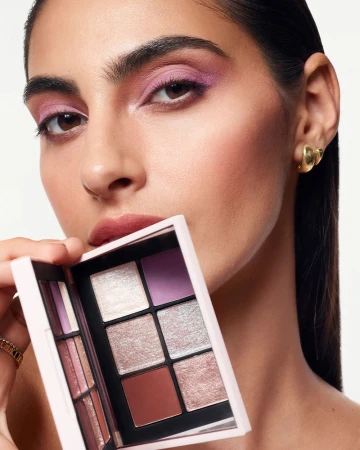 Close-up of a woman holding an eyeshadow palette, showcasing pink and neutral makeup. Beauty shot against a clean white background.
