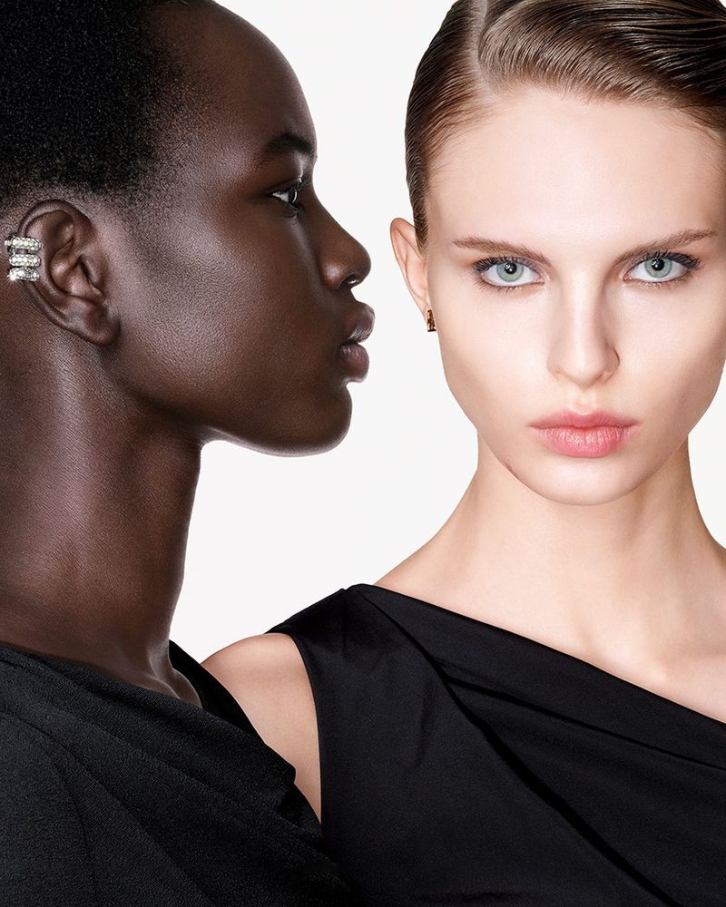 Close-up of two women of different ethnicities in black dresses posing in front of a white backdrop for a beauty and fashion shot.