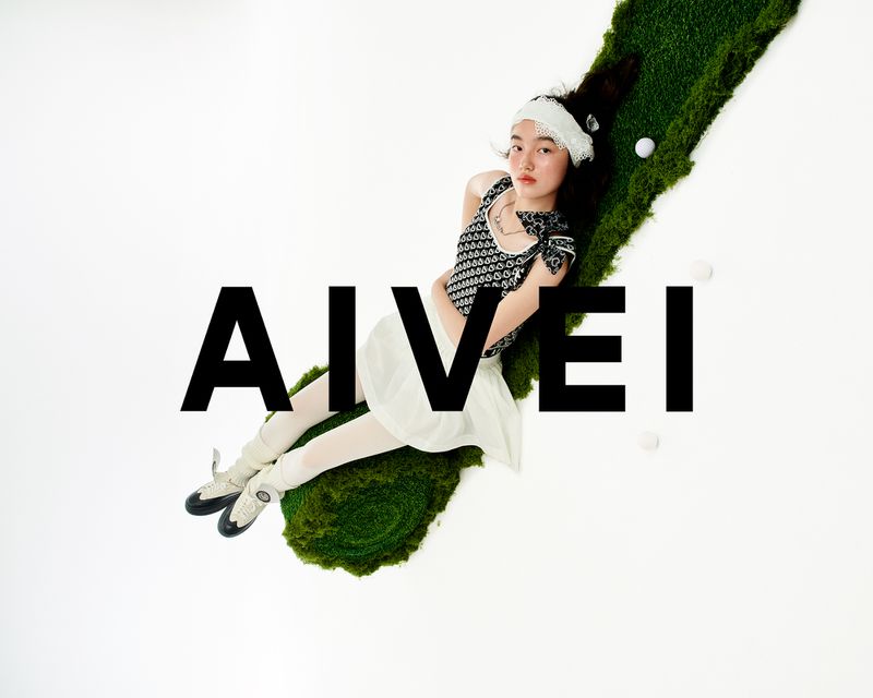 Young woman lies on a mossy surface in black-and-white patterned top, white skirt, and ballet shoes, accented by golf balls.