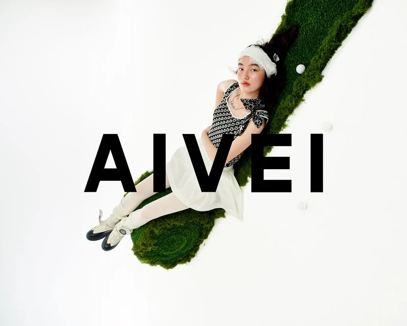 Young woman lies on a mossy surface in black-and-white patterned top, white skirt, and ballet shoes, accented by golf balls.