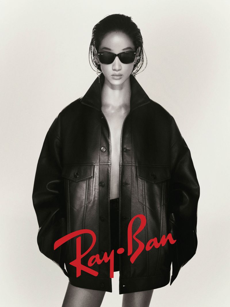 Fashion shot of a female model in a leather jacket and sunglasses, posing against a light background with the Ray-Ban logo visible.