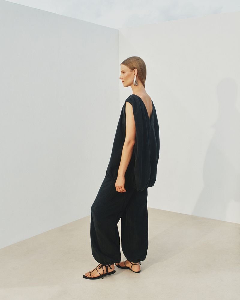 Model Suvi Riggs wearing a black sleeveless top and matching trousers against a white seamless background for Another Tomorrow S/S 25.