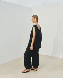 Model Suvi Riggs wearing a black sleeveless top and matching trousers against a white seamless background for Another Tomorrow S/S 25.