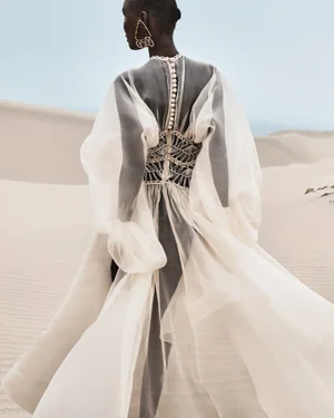 Model Abény Nhial wearing a sheer white dress with billowing sleeves in sand dunes for Zimmermann S/S 2025 Campaign