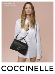 Model Behati Prinsloo wearing a white shirt and holding a black leather handbag against a pink background for Coccinelle S/S 2025 campaign.