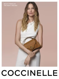 Model Behati Prinsloo holding a brown leather handbag, wearing a white sleeveless dress against a neutral pink backdrop.