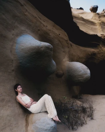 Model wearing a cream crochet outfit seated against eroded rock formations for Escvdo S/S 25 campaign photographed by Diego Bendezu.