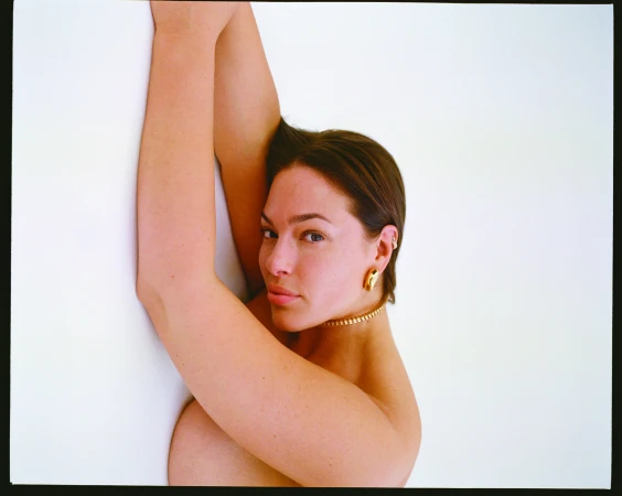 Close-up portrait of Ashley Graham with arms raised against a white wall for Love Want magazine.