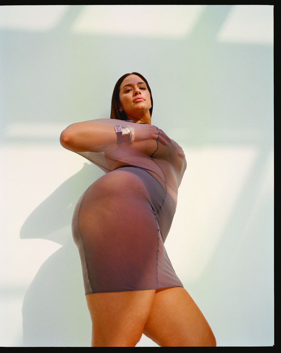Studio shot of an adult female posing in a translucent grey dress against a plain white backdrop, with a low angle view.