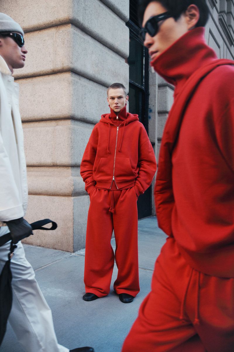 Three fashion models on a city sidewalk wear matching red and white sweatsuits and black shoes, with a modern urban backdrop.