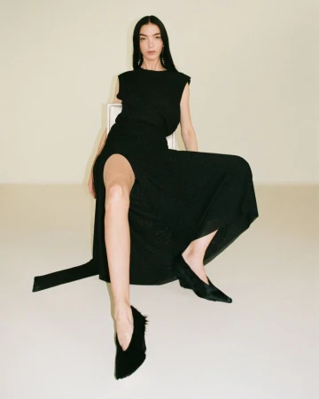 Model Mariacarla Boscono seated on a chair wearing a black dress for Camilla and Marc S/S 2025 campaign