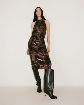 A woman poses in a sparkly dress and knee-high boots against a white background, captured in a full shot fashion studio setting.