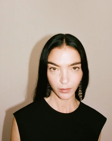 Portrait of model Mariacarla Boscono wearing a black top and statement earrings against a neutral background