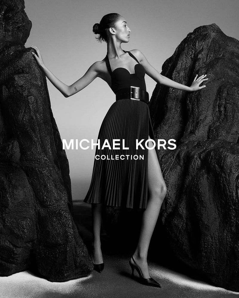 Mona Tougaard in a black halter dress and wide belt posing between rock formations for Michael Kors Collection