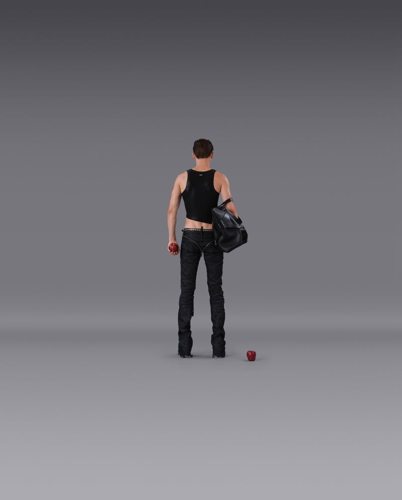 Male figure in black tank top and jeans holds a red apple and black duffel bag against a neutral gray background in a studio setting.