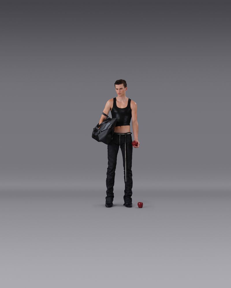 Full shot of a man in black tank top and pants holding a duffel bag, posing in a minimalist grey photo studio with a solitary apple.