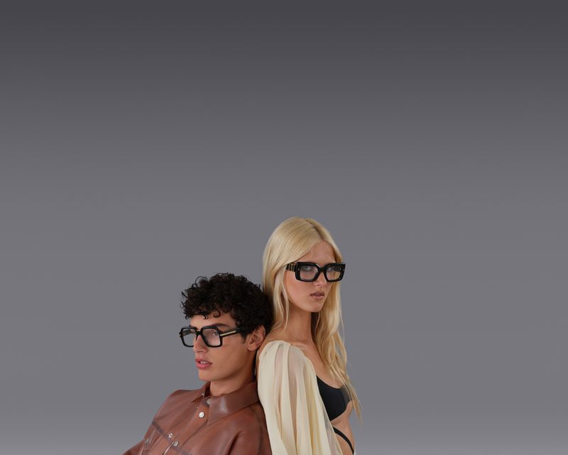 Two models wearing thick black frame glasses against a seamless grey backdrop for Dsquared2 S/S 2025 campaign.