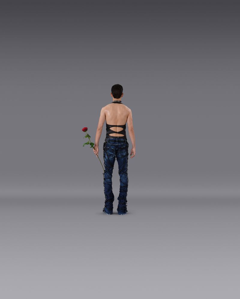 Adult male holding a rose and wearing blue jeans and black top. Indoor studio setting with soft lighting and gray background.
