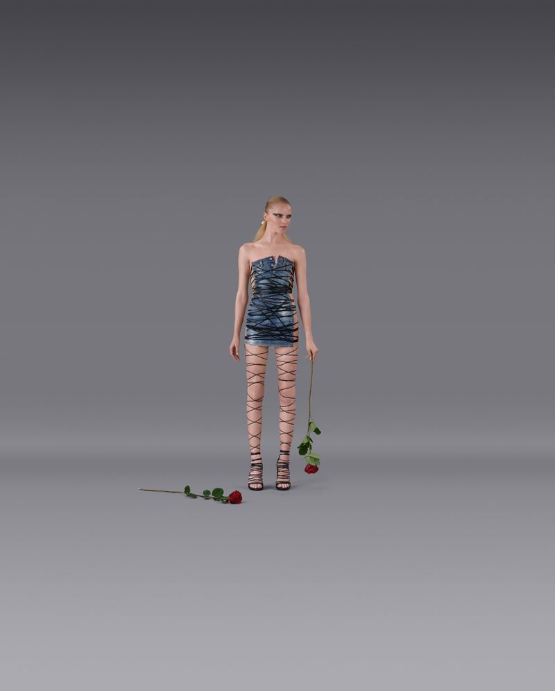 A blonde fashion model in a blue strapless mini-dress and lace-up high heels poses in a studio holding red roses in a full shot.