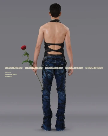 Back view of a slender person in dark halter top and laced jeans holding a rose, studio lit against a gray background for a fashion shoot.