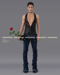 Man wearing a black leather vest and distressed denim jeans holding a red rose against a grey background.