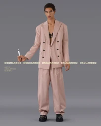 Man wearing a pink double-breasted suit holding a white marker against a plain grey studio backdrop