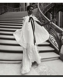 Model wearing a white dress with a black bow on a grand staircase for Chanel SS25